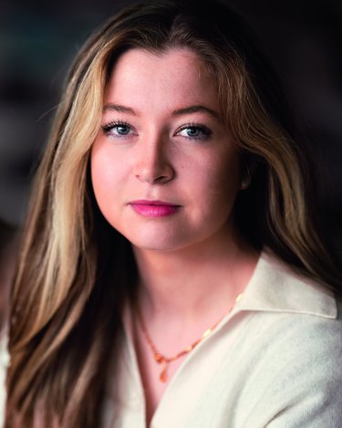 Zwei Frauen mit unterschiedlichen Haarfarben, eine mit rotem Haar und die andere mit blonden Locken, posieren in einem neutralen Umfeld.