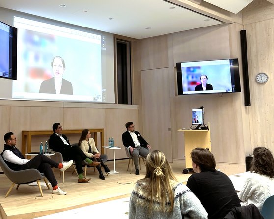 A discussion panel with four people sitting on stage while one person is connected via a screen.