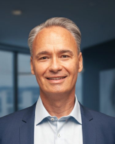 Ein Mann in einem blauen Anzug und Hemd steht lächelnd vor einem modernen Bürohintergrund.