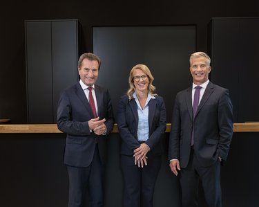 Frau Dr. Dorothée Hofer, Geschäftsführerin der EBS Universität, Günther H. Oettinger, Präsident der EBS Universität, und Prof. Dr. Henning Werner, Rektor der EBS Universität, stehen vor dem Empfangstresen und lächeln freundlich.