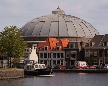 Round, gray dome building over a canal, surrounded by historic houses and a boat passing by.
