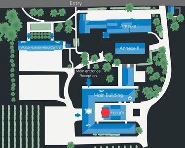 Site plan of an area featuring various buildings, including the main building, reception, and forum, surrounded by green spaces and vineyards. Entrances are clearly marked, and the arrangement of the buildings is presented schematically.