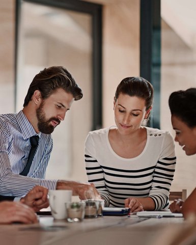 Four people in a meeting room are discussing documents and notes while sitting at a table.