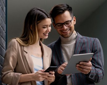 Frau und Mann auf Tablet schauend neben einer schwarzen Wand