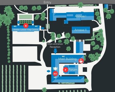 Site plan of an area with various buildings, including the main building, a forum, and a reception area. Markings indicate entrances and key points, surrounded by green spaces and vineyards.