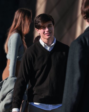 Eine Gruppe junger Menschen steht im Freien. Ein Junge in einem schwarzen Pullover spricht mit einem anderen, während zwei Mädchen im Hintergrund stehen.
