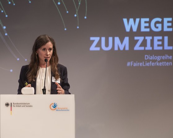 Eine Frau spricht am Rednerpult bei einer Veranstaltung mit dem Titel "Wege zum Ziel" zur Dialogreihe #FaireLieferketten.