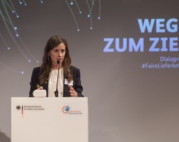 Eine Frau spricht am Rednerpult bei einer Veranstaltung mit dem Titel "Wege zum Ziel" zur Dialogreihe #FaireLieferketten.