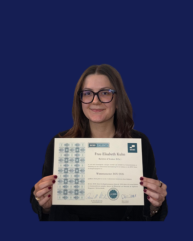Frau Elisabeth Kuhn hält ein Zertifikat in der Hand, das ihren Abschluss als Bachelor of Science aus dem Wintersemester 2015/2016 bestätigt.