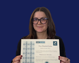 Frau Elisabeth Kuhn hält ein Zertifikat in der Hand, das ihren Abschluss als Bachelor of Science aus dem Wintersemester 2015/2016 bestätigt.