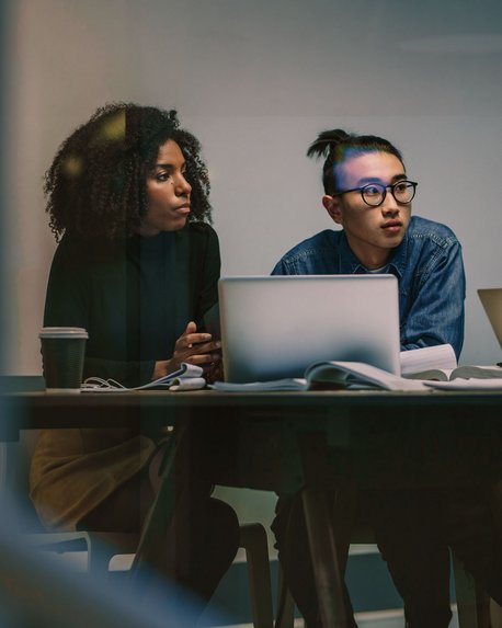Vier Personen sitzen an einem Tisch mit Laptops und Notizen, während sie sich in einer Besprechung austauschen. Die Gruppe besteht aus zwei Frauen und zwei Männern, die konzentriert miteinander diskutieren.