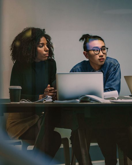Vier Personen sitzen an einem Tisch mit Laptops und Notizen, während sie sich in einer Besprechung austauschen. Die Gruppe besteht aus zwei Frauen und zwei Männern, die konzentriert miteinander diskutieren.