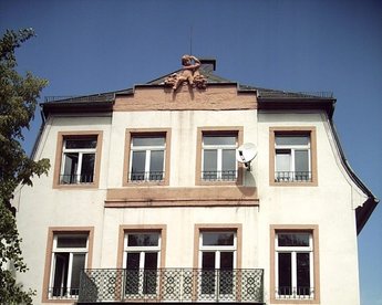 Dreigeschossiges Gebäude mit Balkon, Fenster im klassischen Stil und einem dekorativen Element an der Fassade.