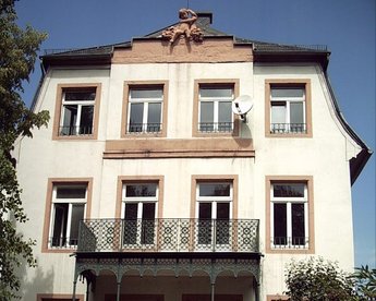 Three-story building with a balcony, windows in a classic style, and a decorative element on the facade.