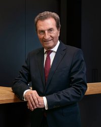 A man in a suit stands at a wooden bar, smiling, with a modern backdrop in dark colors.