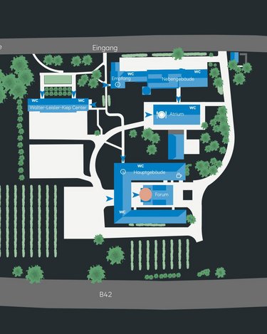 Lageplan eines Geländes mit verschiedenen Gebäuden, Eingängen, Grünflächen und einem Parkplatz. Beschriftungen zeigen Funktionen der einzelnen Bereiche.