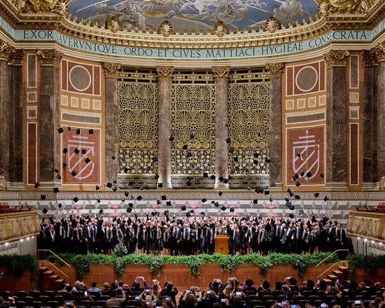 Ein großer Chor steht auf der Bühne eines prächtigen Konzertsaals, umgeben von aufwendiger Architektur und Dekoration.