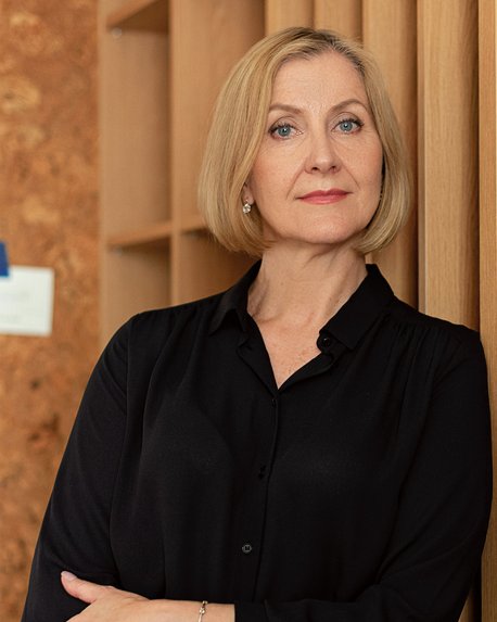 Eine Frau mit blonden Haaren in einem schwarzen Oberteil steht neben einem Bücherregal, das eine dekorative Vase enthält.